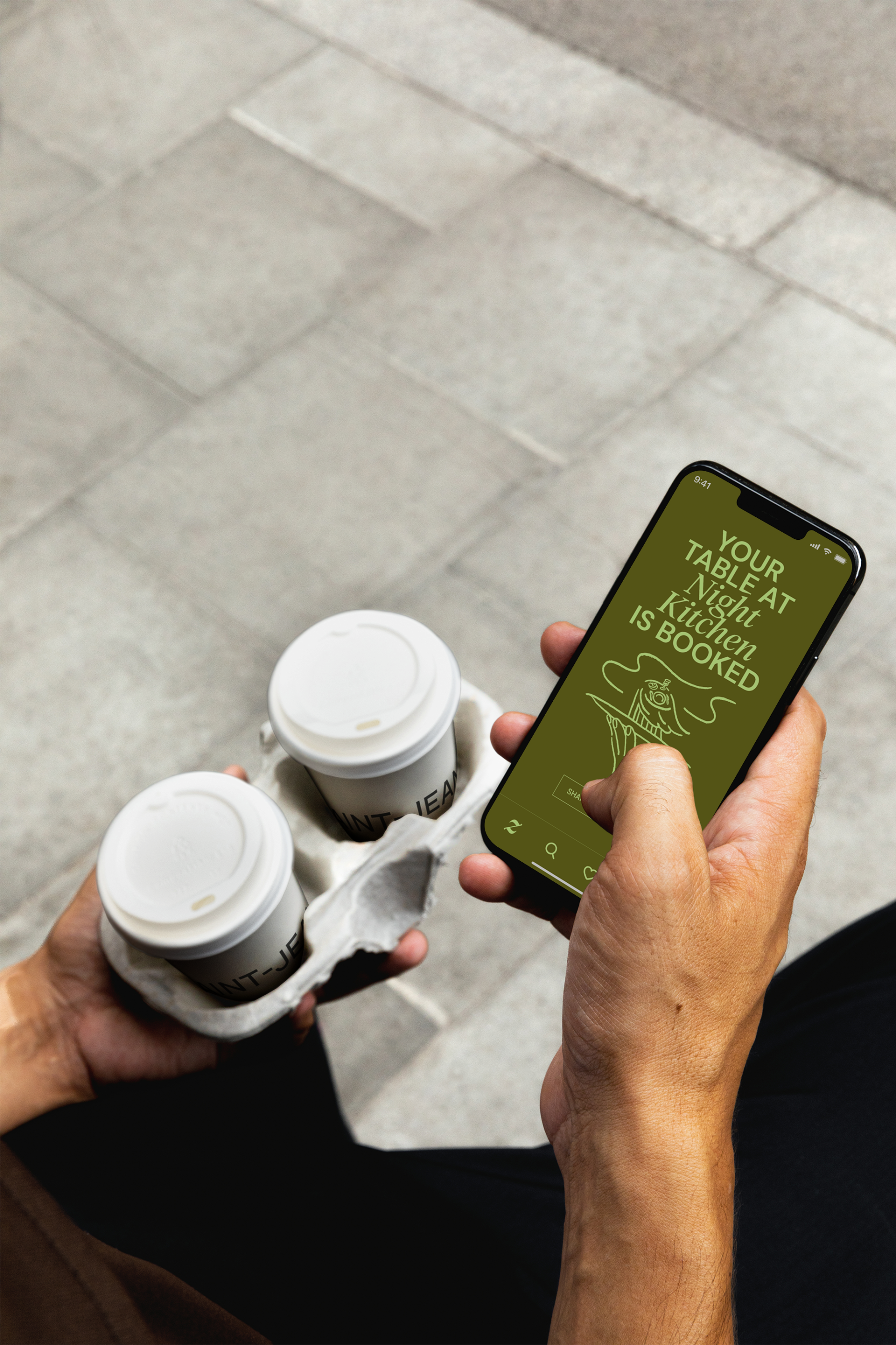 Overhead mockup of a person holding a phone showing the Zenchef confirmation 'Your table at Night Kitchen is booked,' alongside two takeaway coffee cups in a tray, on a sidewalk.
