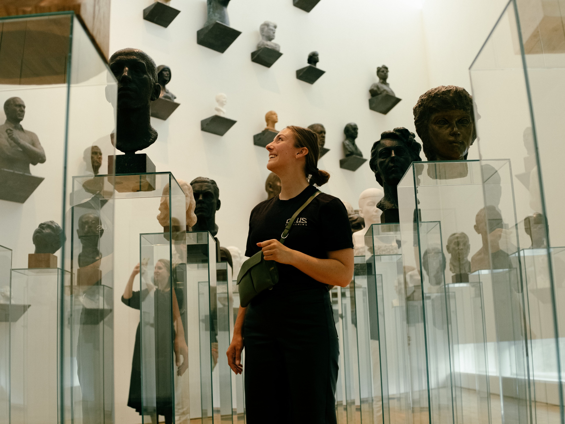 Eveline Koppejan looking up at sculptured portrait busts in glass displays at a Tallinn art museum