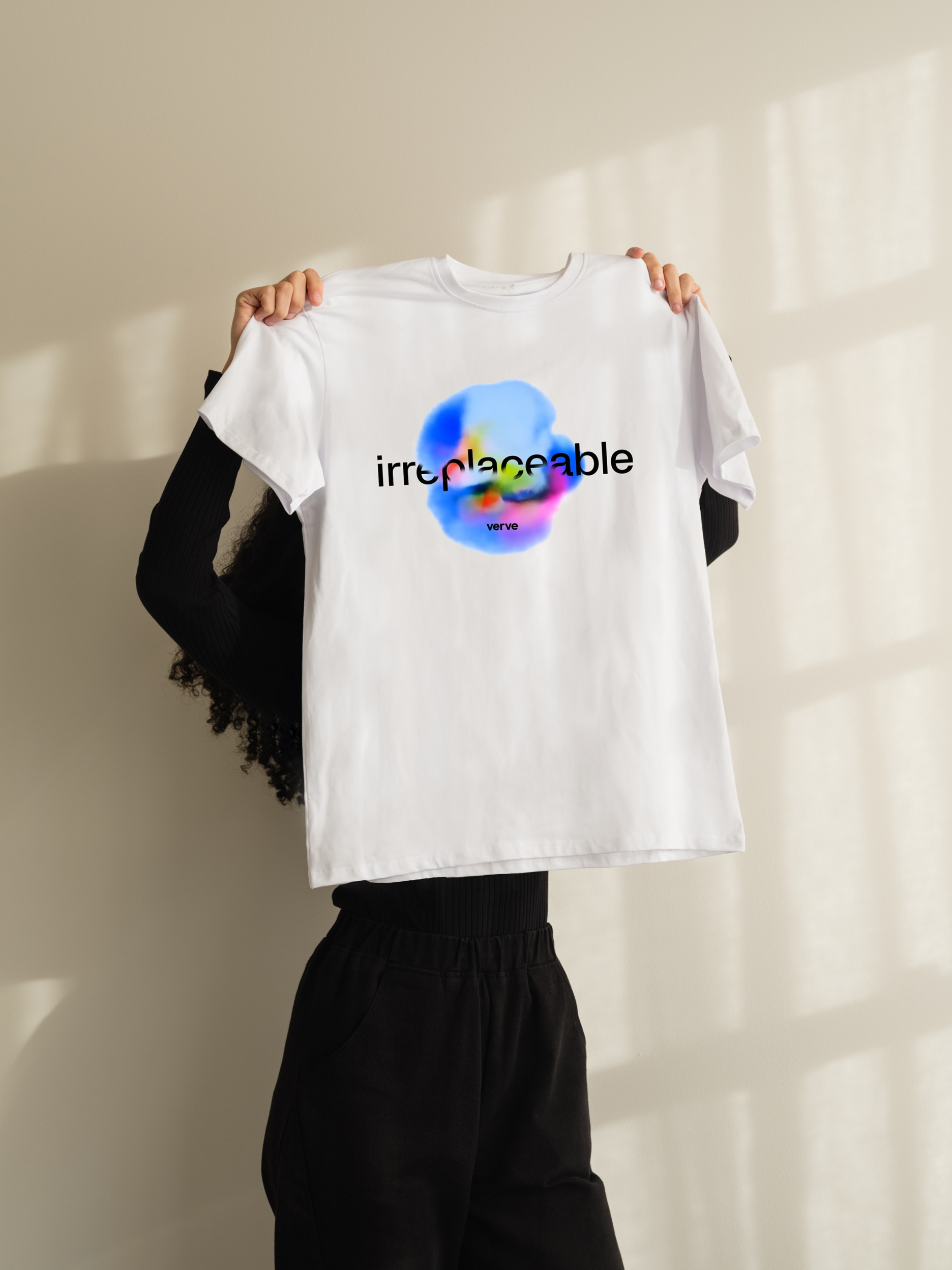 Apparel mockup of person holding white Verve t-shirt featuring colorful graphic and the word irreplaceable